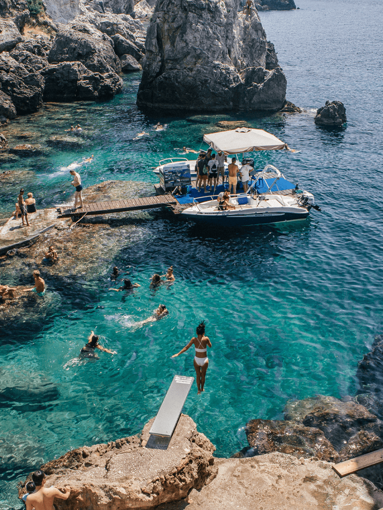 Swimmers enjoying turquoise water near rocky coastline with a boat and dock at a scenic seaside destination.