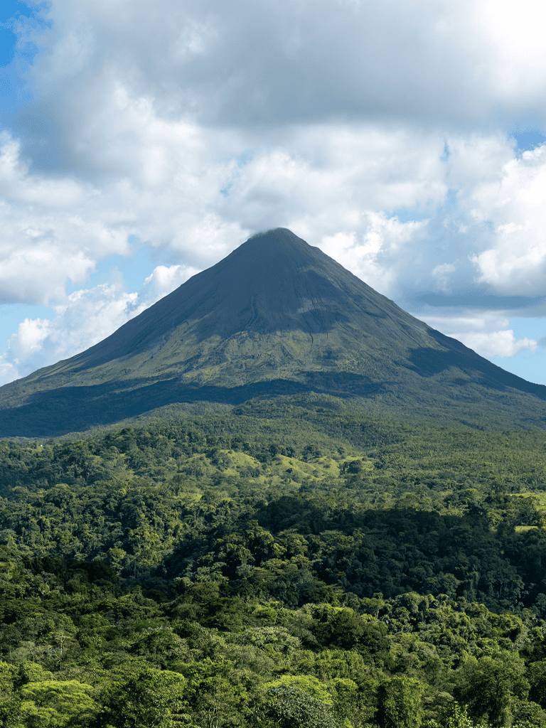 Lush green rainforest with a majestic volcano in the background, under a partly cloudy sky.