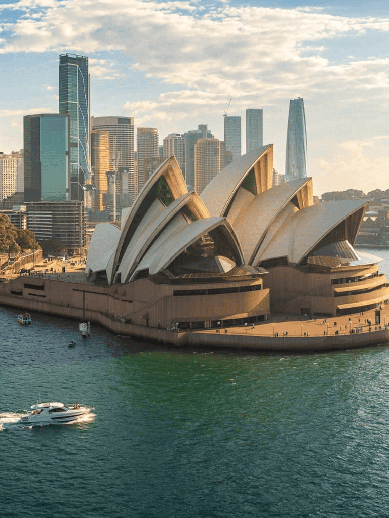 Sydney Opera House with city skyline at sunset, iconic Australian landmark.