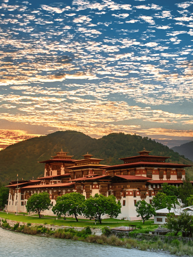 Vast mountain landscape with traditional Bhutanese architecture and vibrant sunset sky.