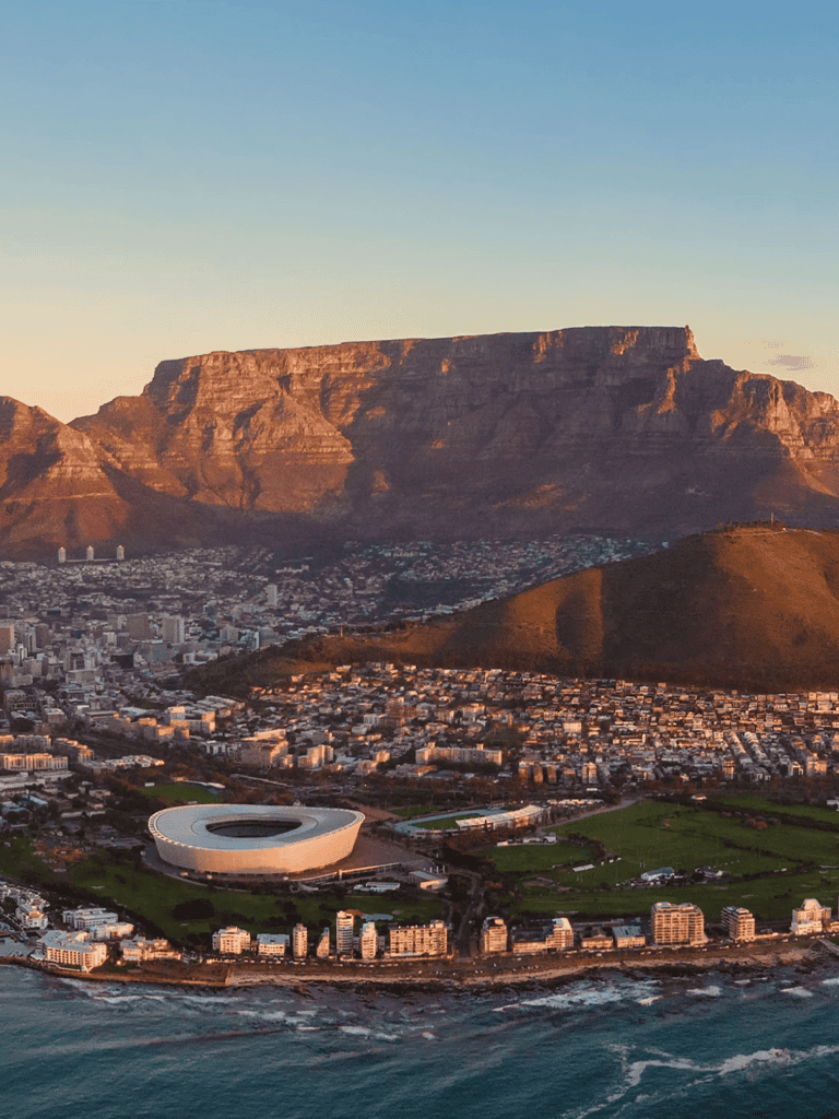 Stunning aerial view of Cape Town, featuring Table Mountain, cityscape, and modern stadium at sunset.