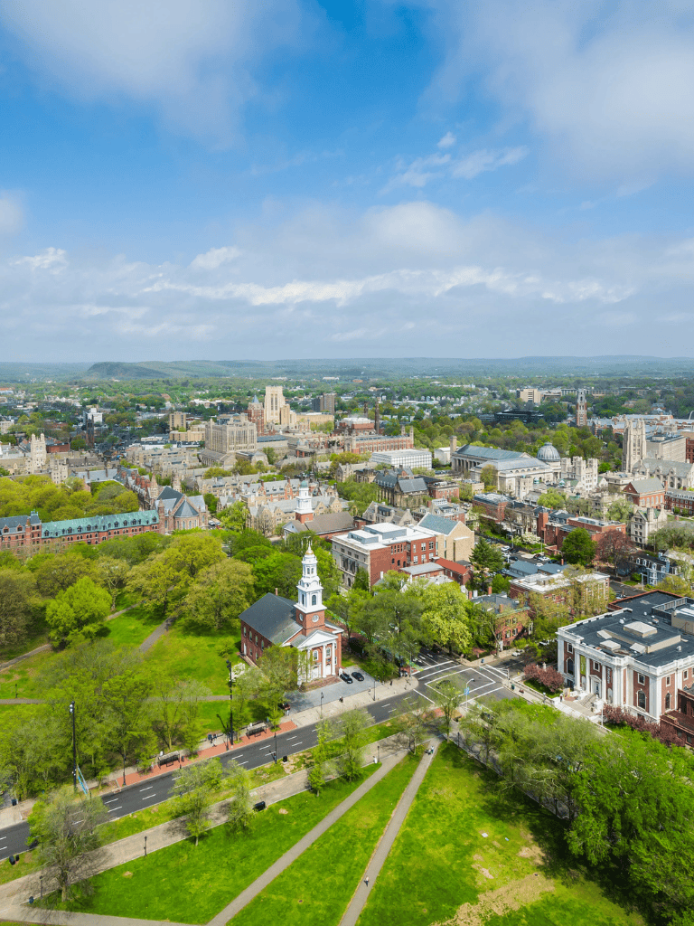 Aerial view of a scenic cityscape with historic buildings, green parks, and mountain background.