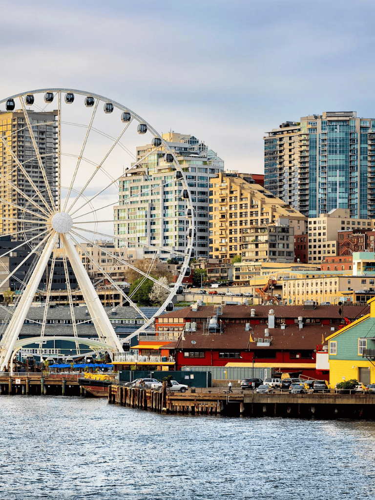 Bright city skyline with waterfront, Ferris wheel, and modern high-rise buildings in Seattle, WA.