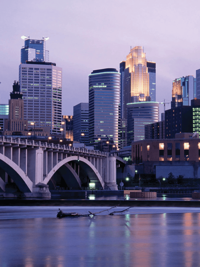 Modern city skyline with tall skyscrapers at dusk, reflecting on the river, highlighting urban development and architecture.