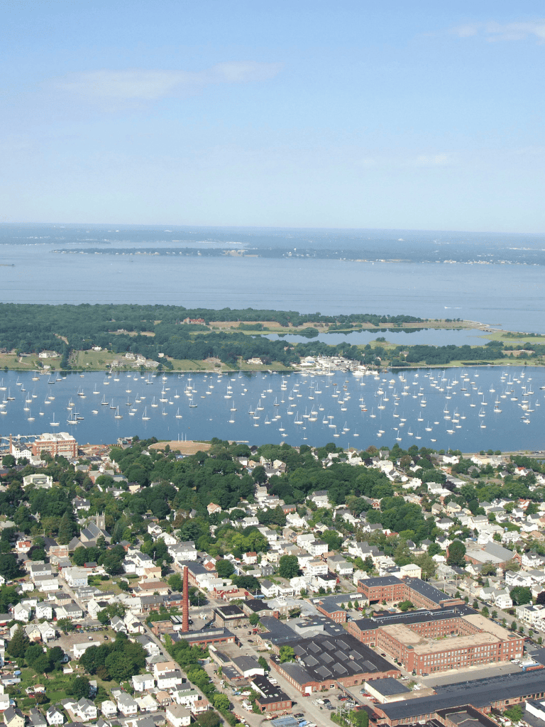 Aerial view of waterfront town with boats, residential area, and scenic water landscape.