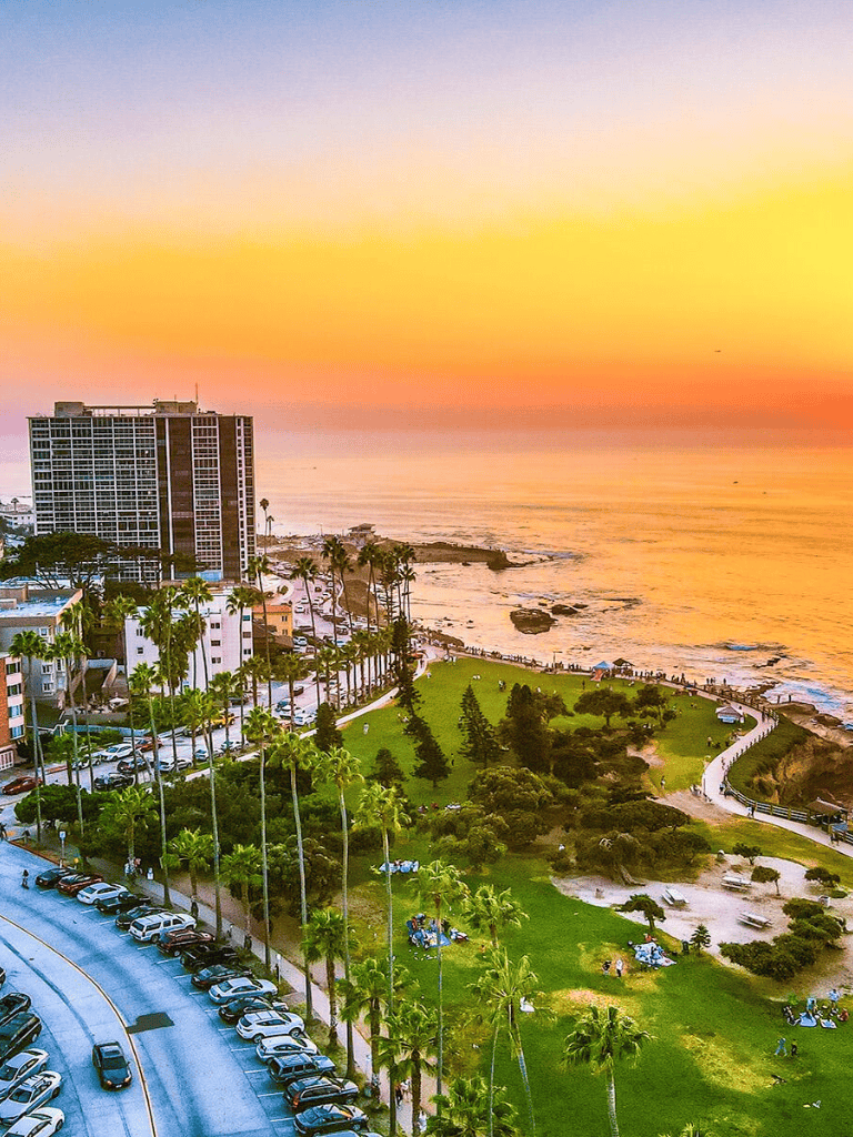 Vibrant sunset over coastal cityscape with palm trees, high-rise buildings, and ocean view, scenic urban beach scene.