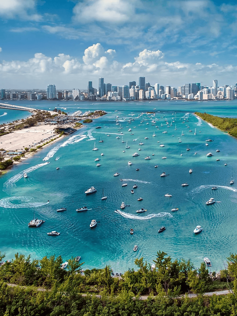 Vibrant city skyline with marina and numerous boats on turquoise water, sunny skies, and lush greenery in Miami, Florida.