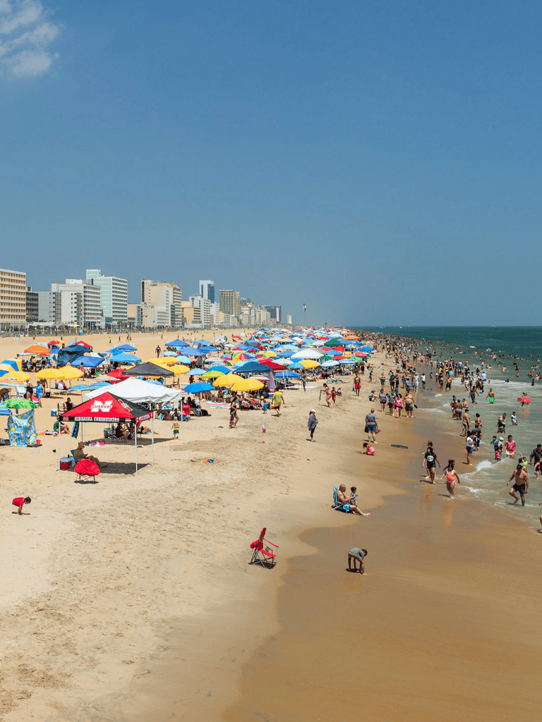 Colorful beach umbrellas on a busy summer shoreline with city skyline in the background.