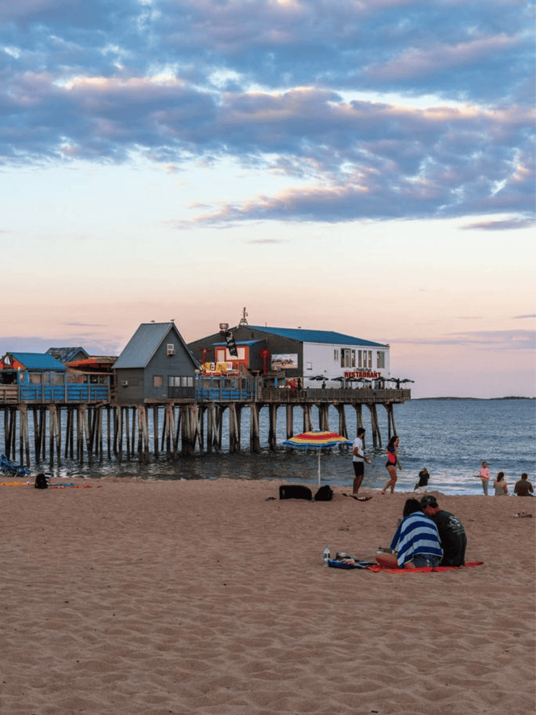 Seaside pier with restaurants and people enjoying the beach during sunset in Ocean City, Maryland.