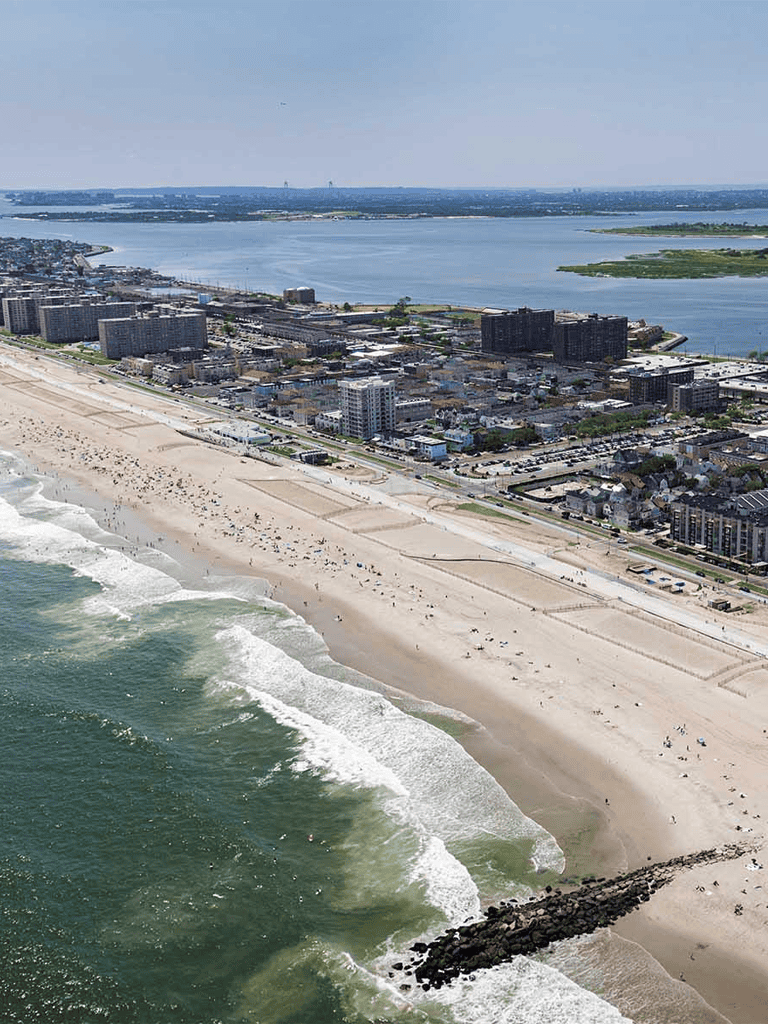 Aerial view of a beach with ocean waves and city buildings in the background.