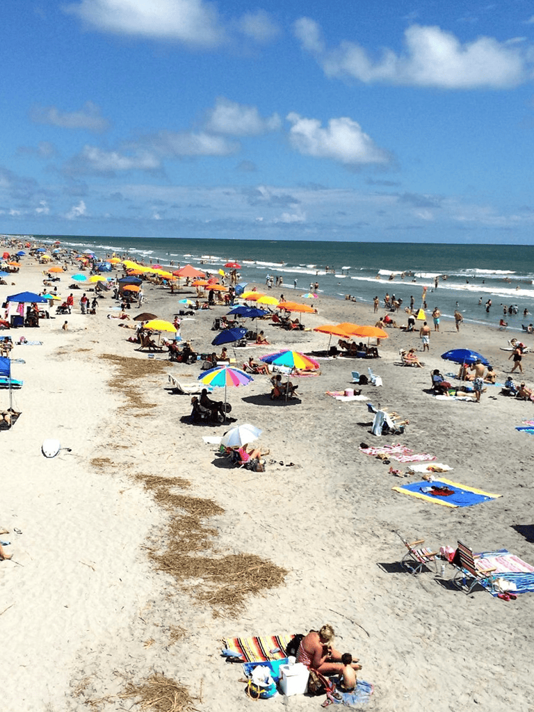 Colorful beach umbrellas and visitors enjoying sunny day at the ocean shoreline.