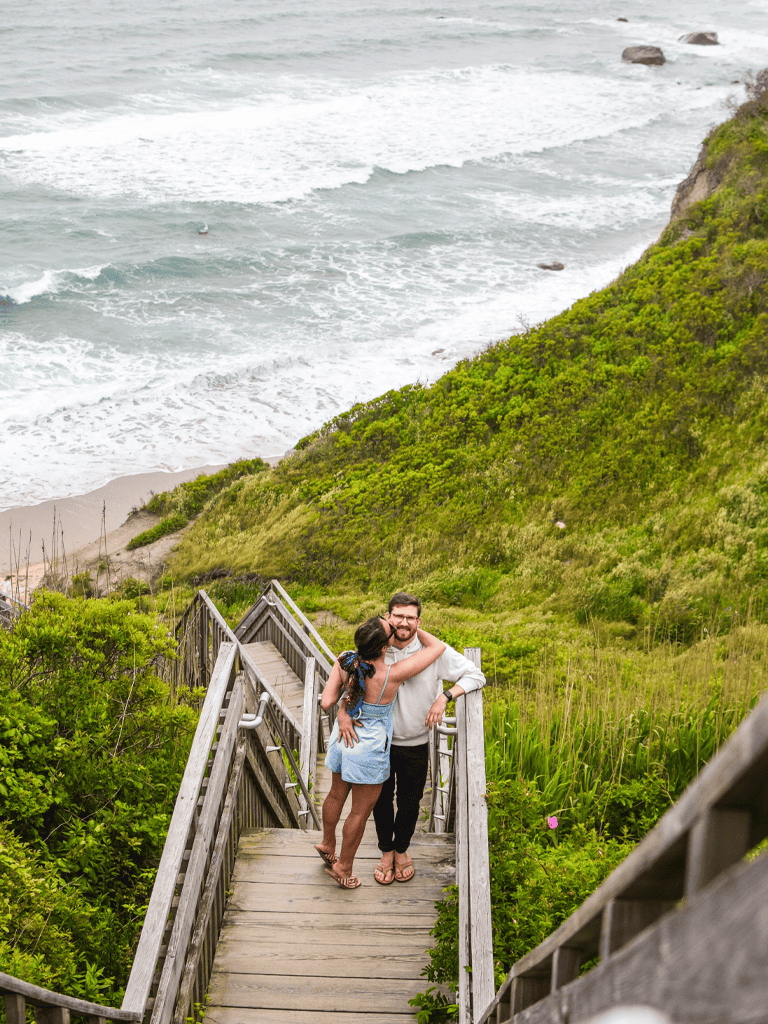Happy couple hugging on beach stairs leading to the coast, scenic ocean view, travel, romantic destination, natural landscape, QuestForDirections.