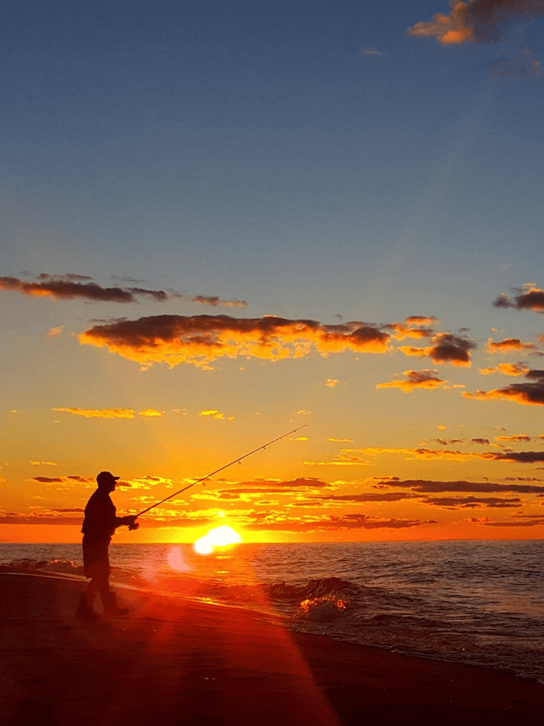 Peaceful sunset beach scene with a person fishing, highlighting outdoor recreation and scenic coastal views.
