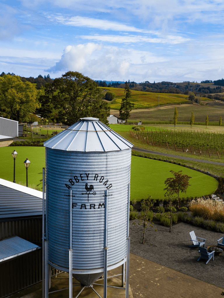 Rustic farm water silo with Abbey Road Farm sign on lush green countryside landscape.