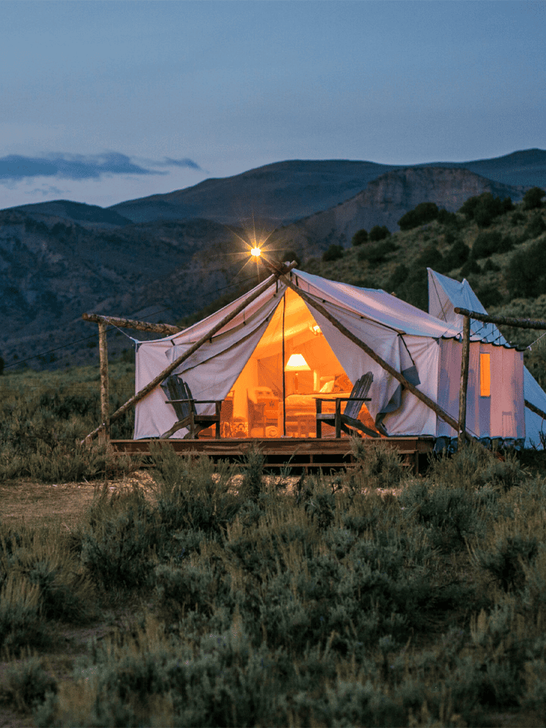 Cozy glamping tent in mountain landscape with warm interior lighting at dusk.