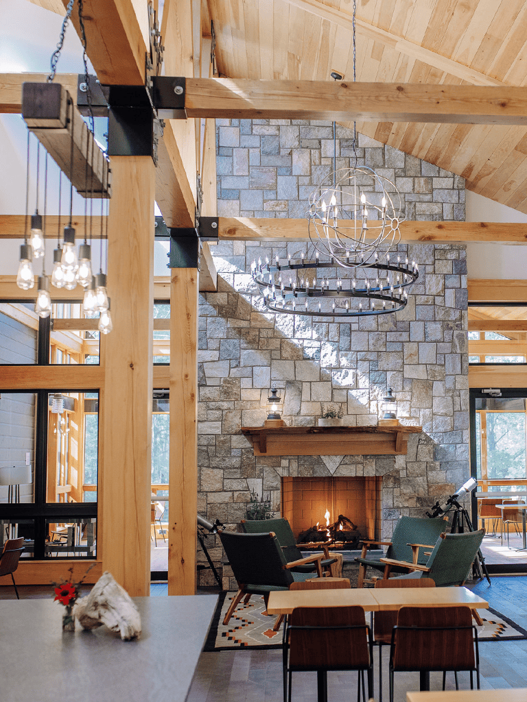 Cozy lodge interior with stone fireplace, wooden beams, and modern chandeliers for relaxation and social gatherings.