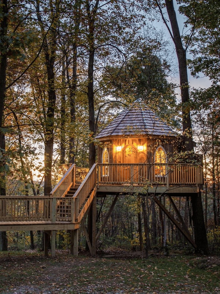 Woodland treehouse with warm lighting, nestled in a forest setting at sunset.