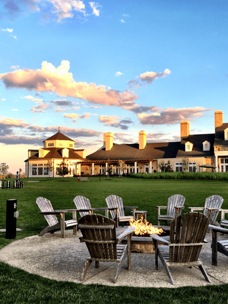 Cozy outdoor fire pit area at dusk with Adirondack chairs, elegant house in the background, perfect for gatherings.