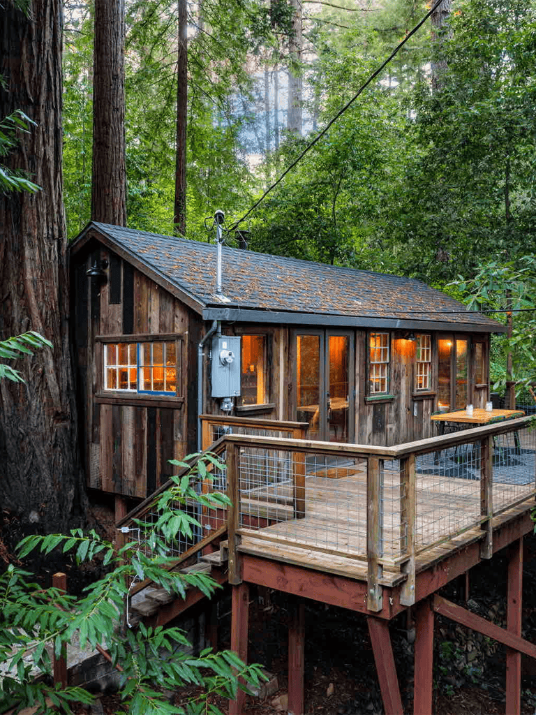 Secluded treehouse cabin nestled in lush forest with wooden deck and large windows, perfect for nature retreats and outdoor adventures.