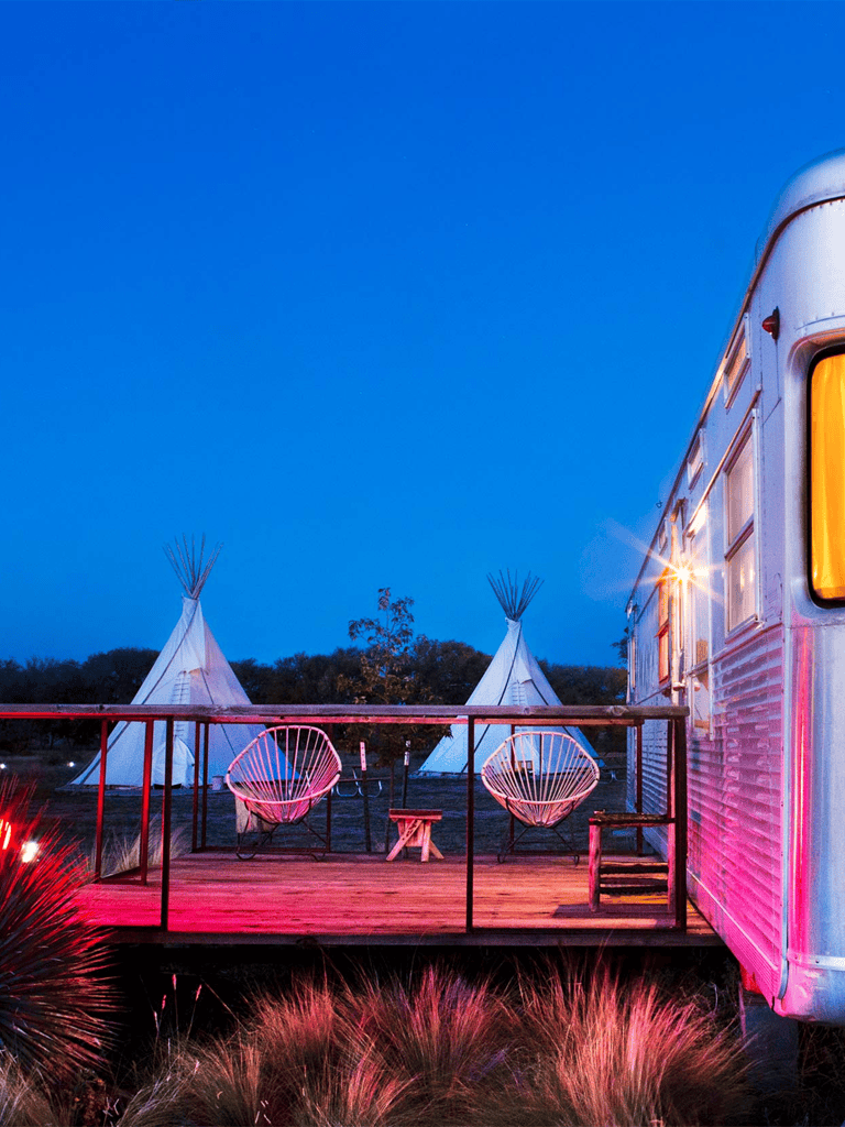 Peaceful glamping site with tipi tents and vintage camper trailer at twilight, perfect for outdoor adventure.