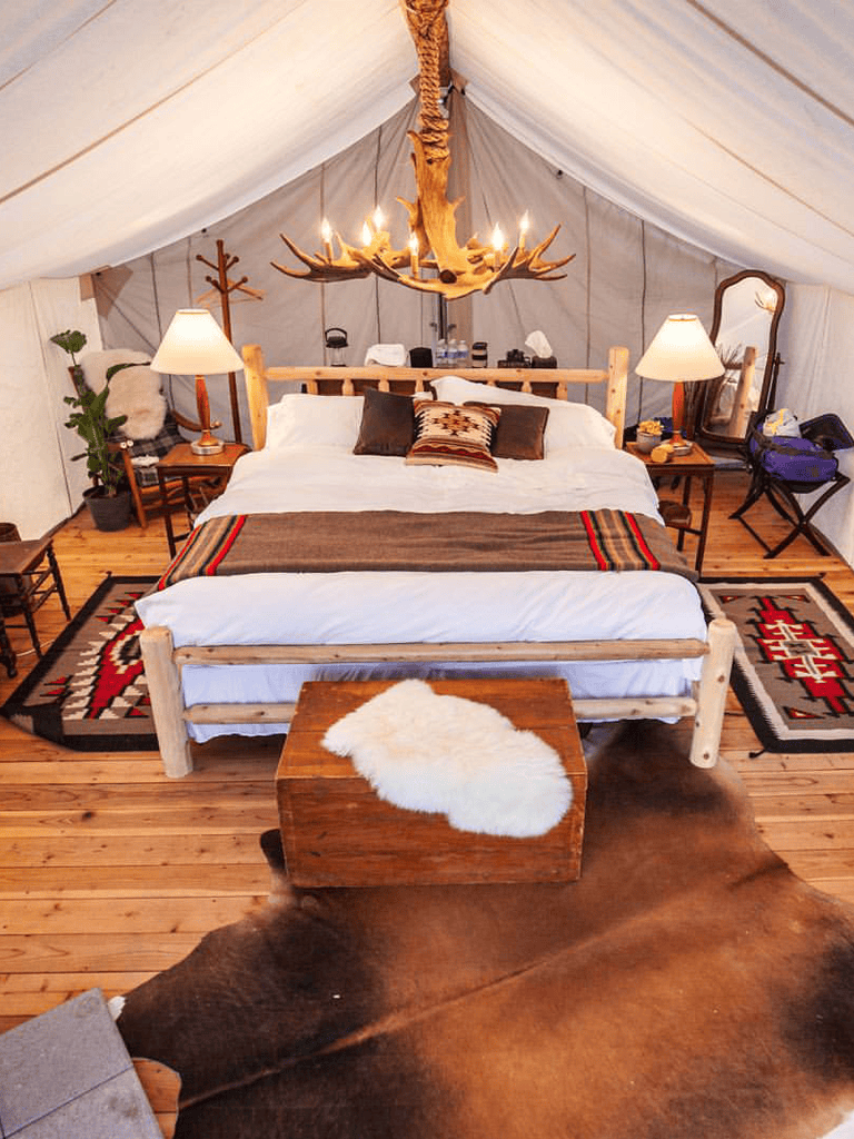 Cozy rustic bedroom with log bed, antler chandelier, and southwestern decor inside a glamping tent.