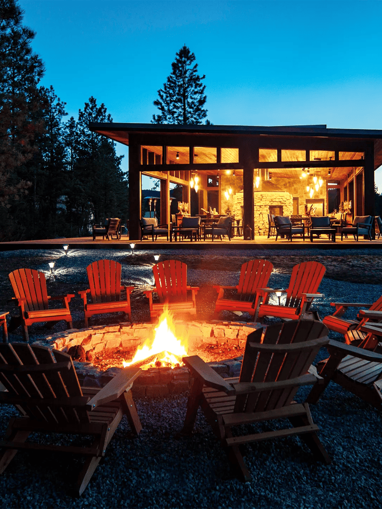 Cozy outdoor fire pit area at a luxury resort with a modern lodge and forest backdrop.