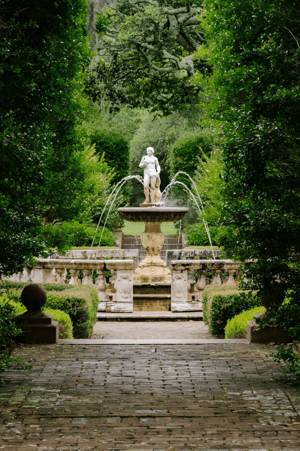 A lush garden with a classical fountain surrounded by greenery and paved pathways, perfect for peaceful outdoor relaxation.