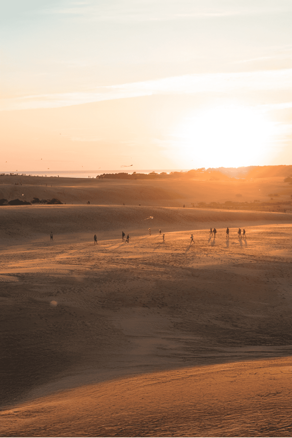 Aerial view of desert dunes at sunset with people walking, scenic landscape for travel and adventure photos.