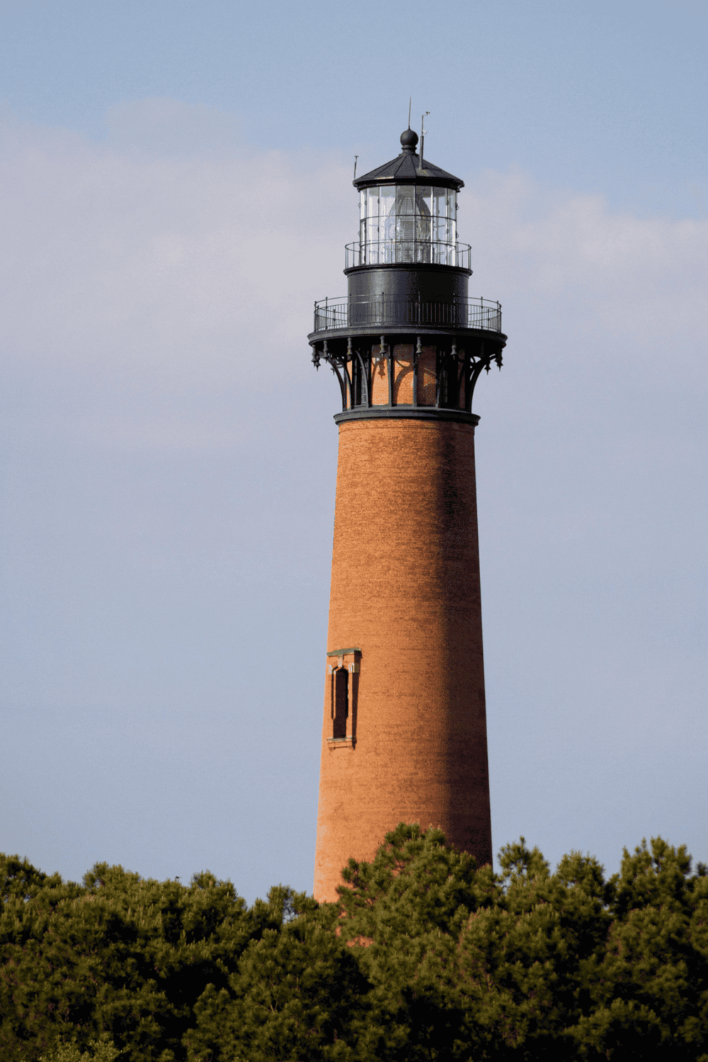 Lighthouse with brick tower and black lantern in daylight, coastal navigation aid.