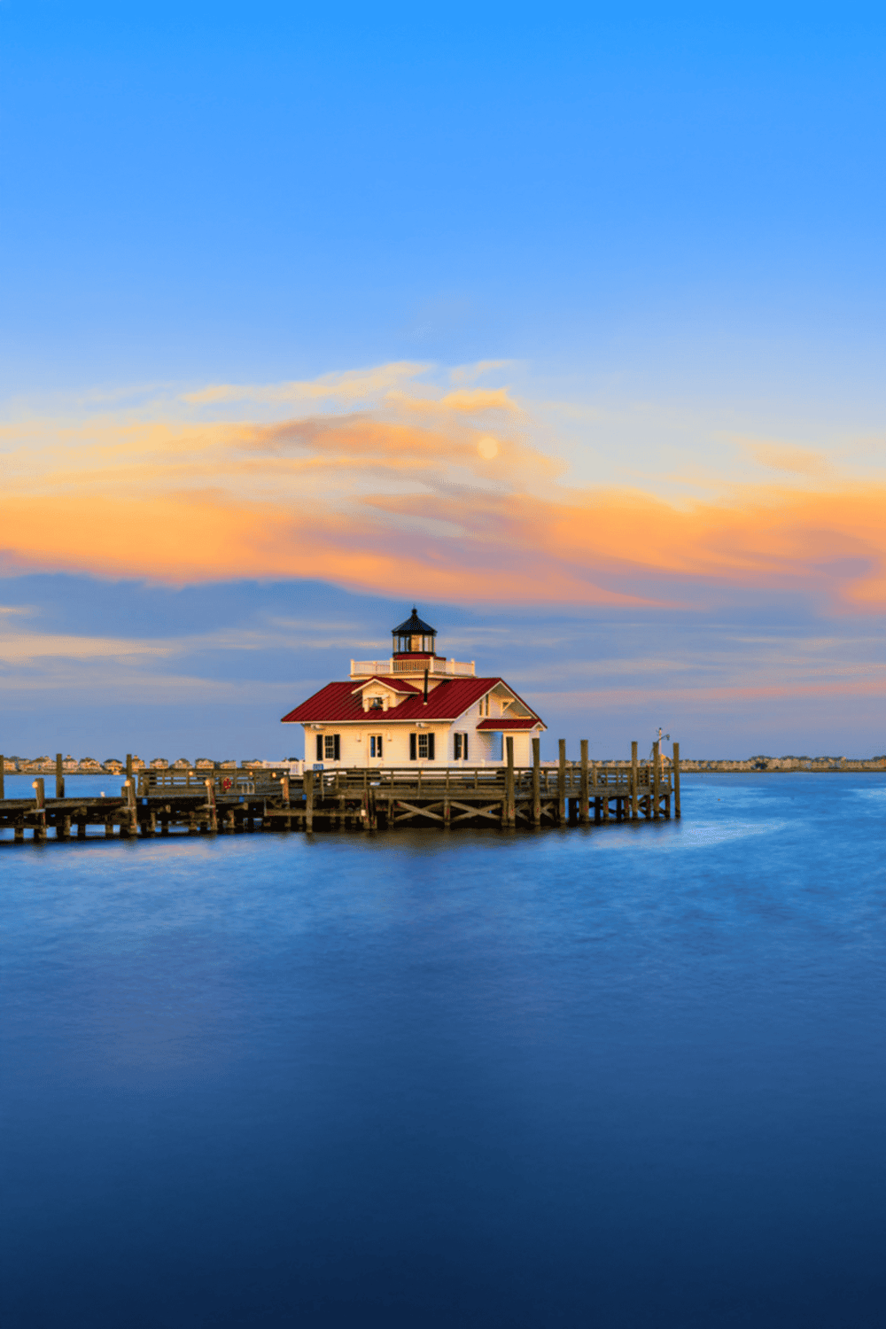 Seaside lighthouse at sunset with vibrant sky and calm water, perfect for coastal navigation and scenic travel.
