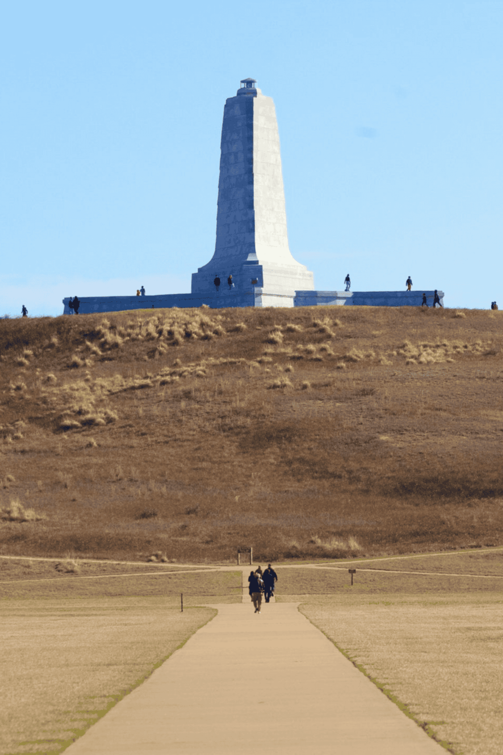 Victorian monument on the hill with people walking towards it, scenic outdoor location, popular travel destination.