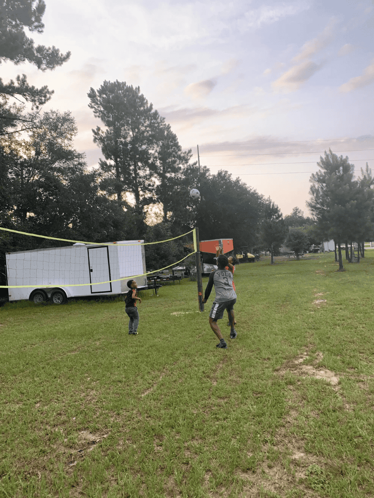Kids playing volleyball outdoors at a park in the evening.