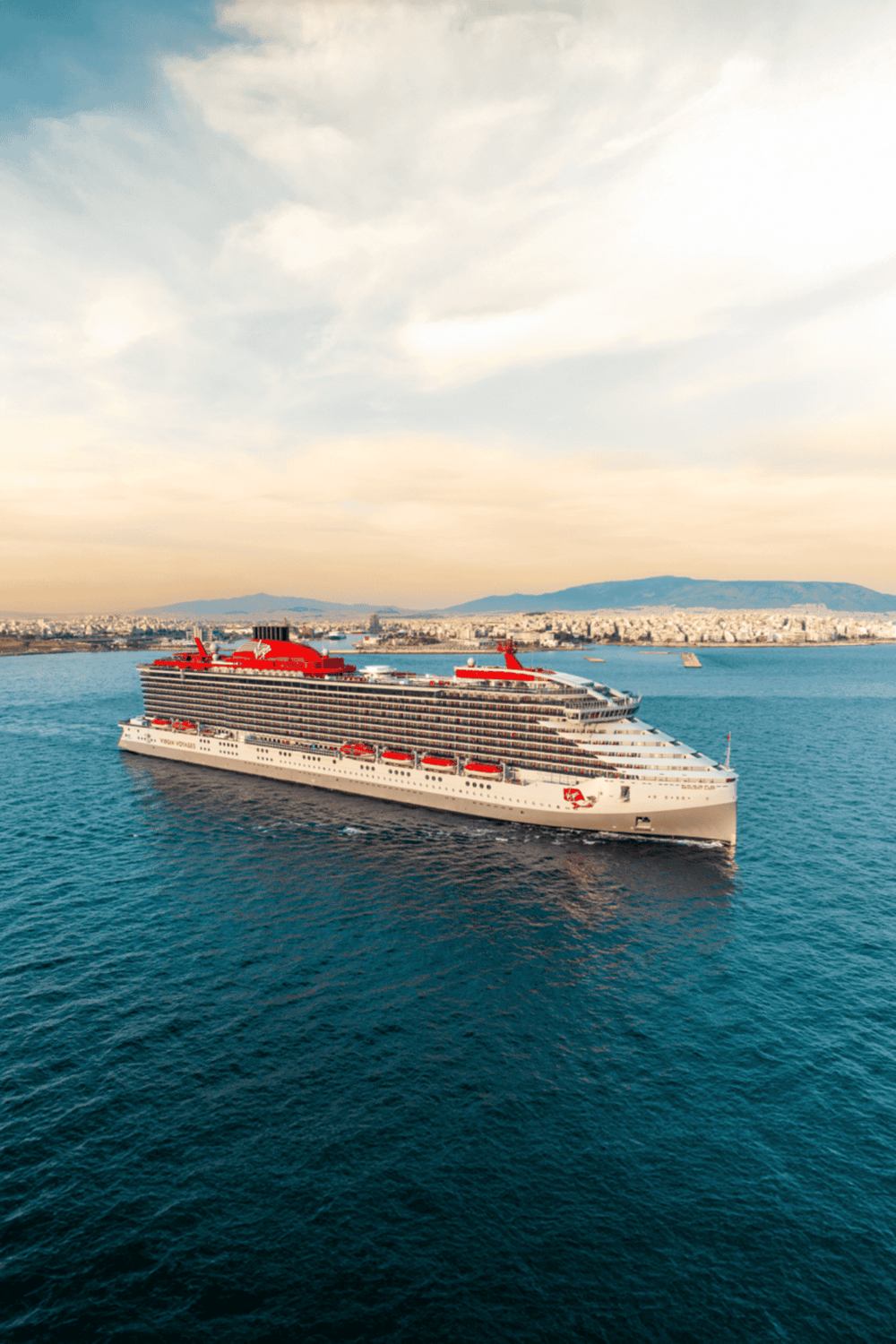 Luxury cruise ship sailing in the ocean with a coastal city in the background, representing travel and vacation cruises.
