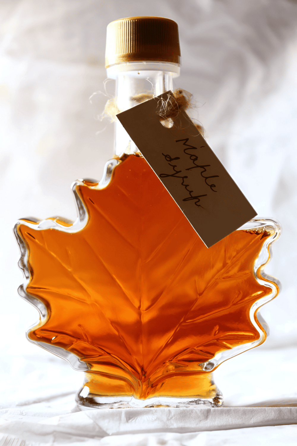 Amber maple syrup bottle in a decorative leaf-shaped glass container.