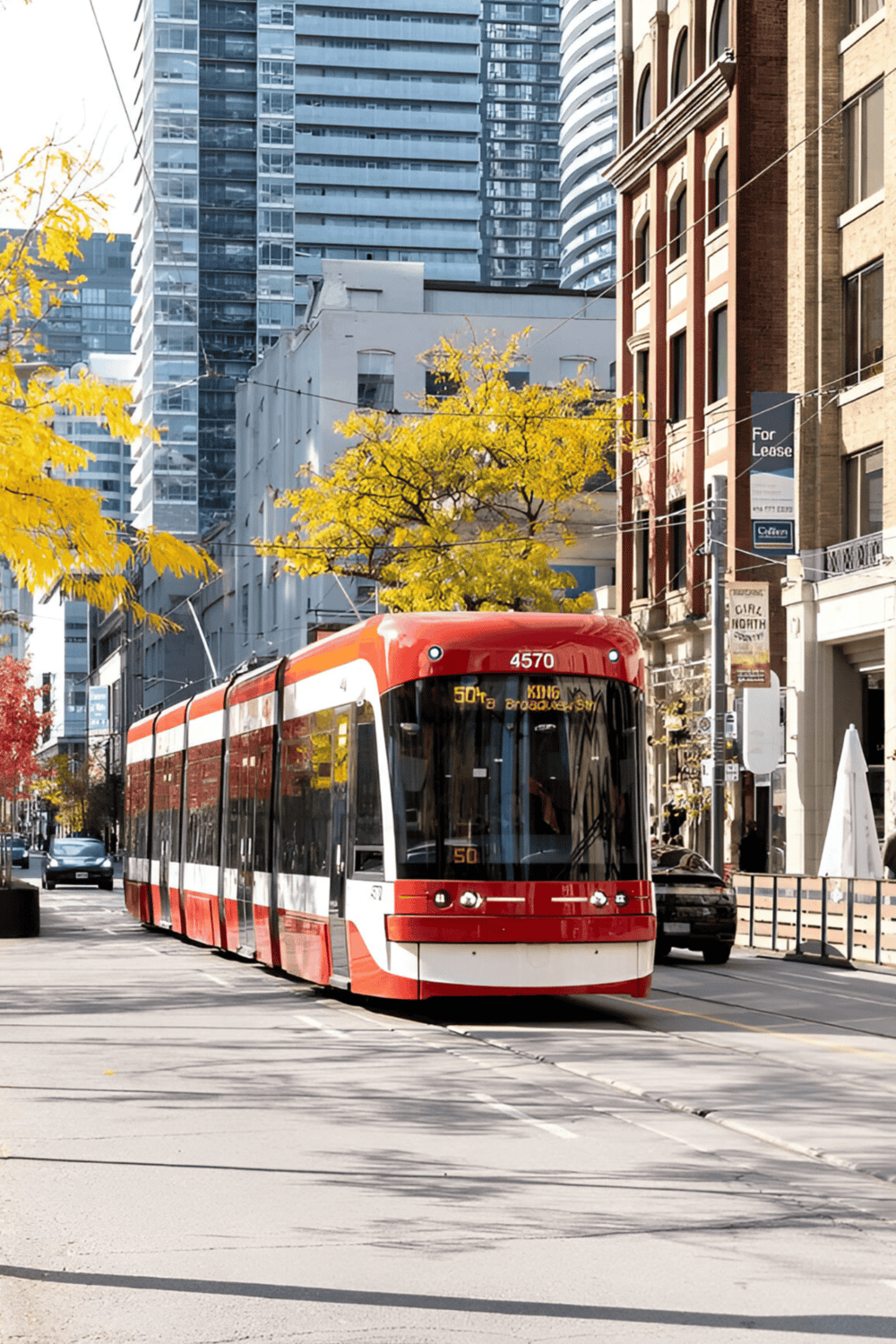 Red streetcar in downtown city with modern high-rise buildings and fall foliage, part of QuestForDirections' urban transit solutions.