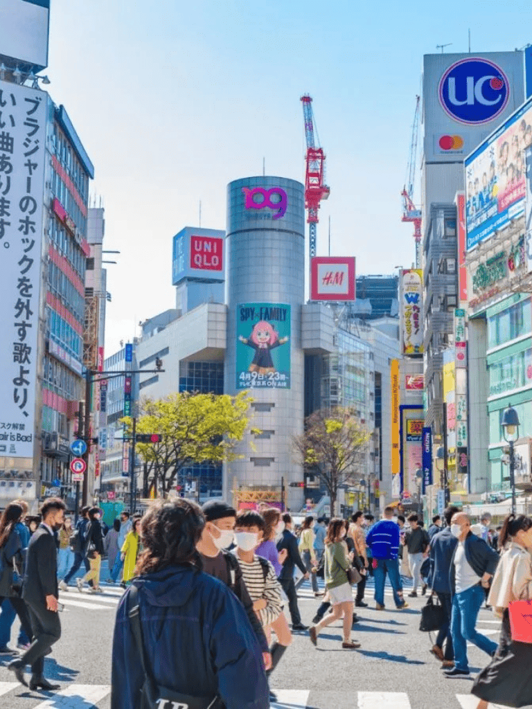 Busy Tokyo crosswalk with shoppers and illuminated billboards in a vibrant urban setting.