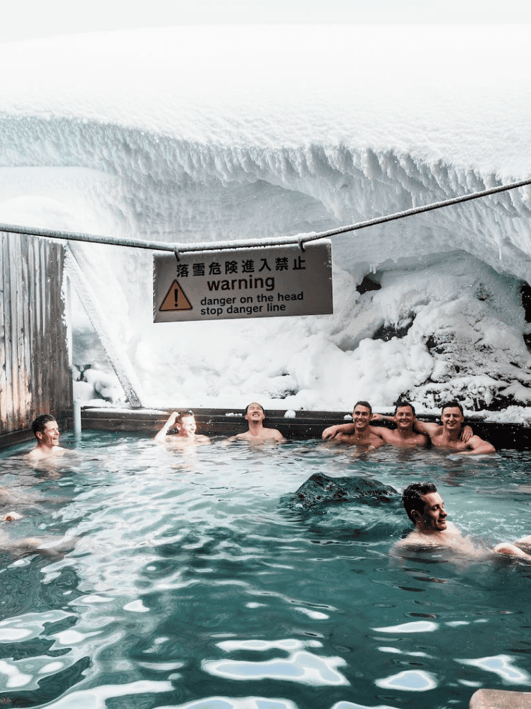 - Snow cave warning sign in icy environment with people enjoying hot spring inside.