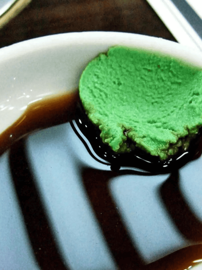 Sweet green matcha sponge cake with chocolate sauce on a white plate, close-up.