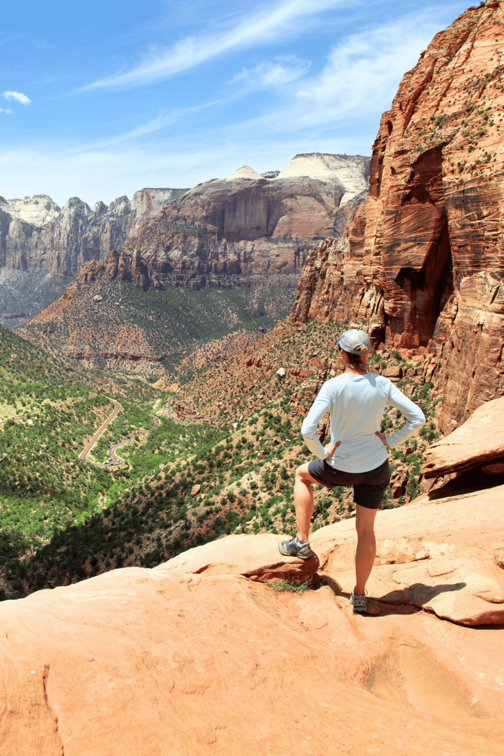 Breathtaking view of Zion Canyon with hiker overlooking red rock cliffs and lush valley below.