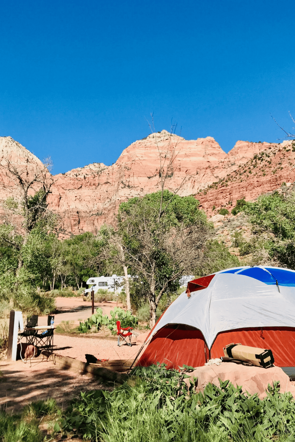 Tent camping at scenic red rock canyon with lush greenery and clear blue sky.