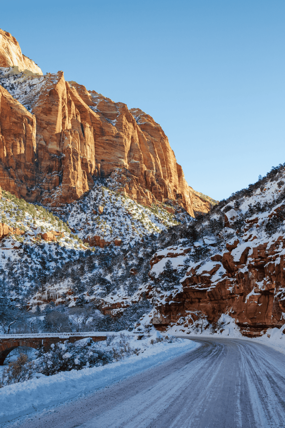 Snowy canyon road with red rock cliffs and clear blue sky, scenic destination for outdoor adventures.