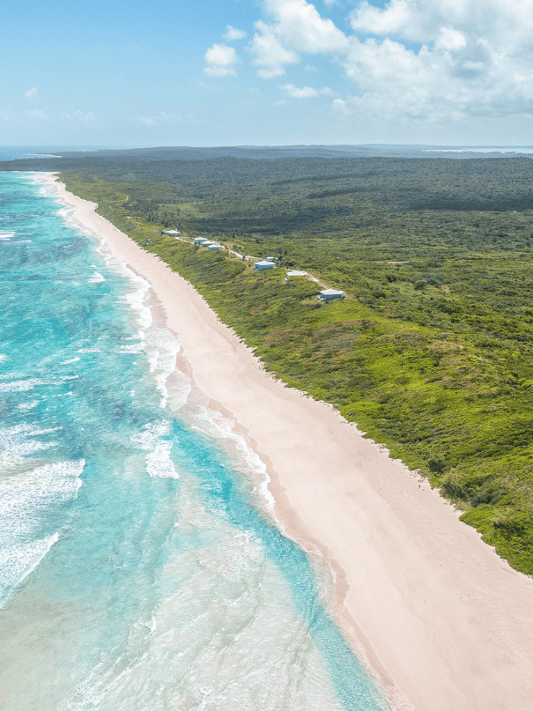 Secluded beach with crystal clear waters and beachfront cottages nestled in lush green coastal landscape.