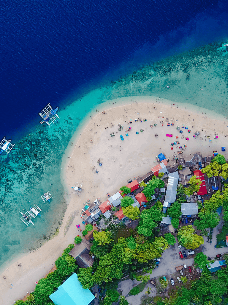 Aerial view of a tropical beach with colorful umbrellas, boats, and lush greenery.