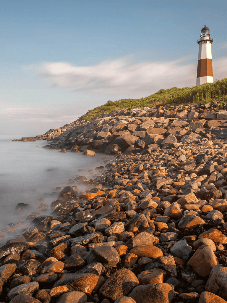 Lighthouse on rocky shoreline at sunset for coastal navigation and travel guides.