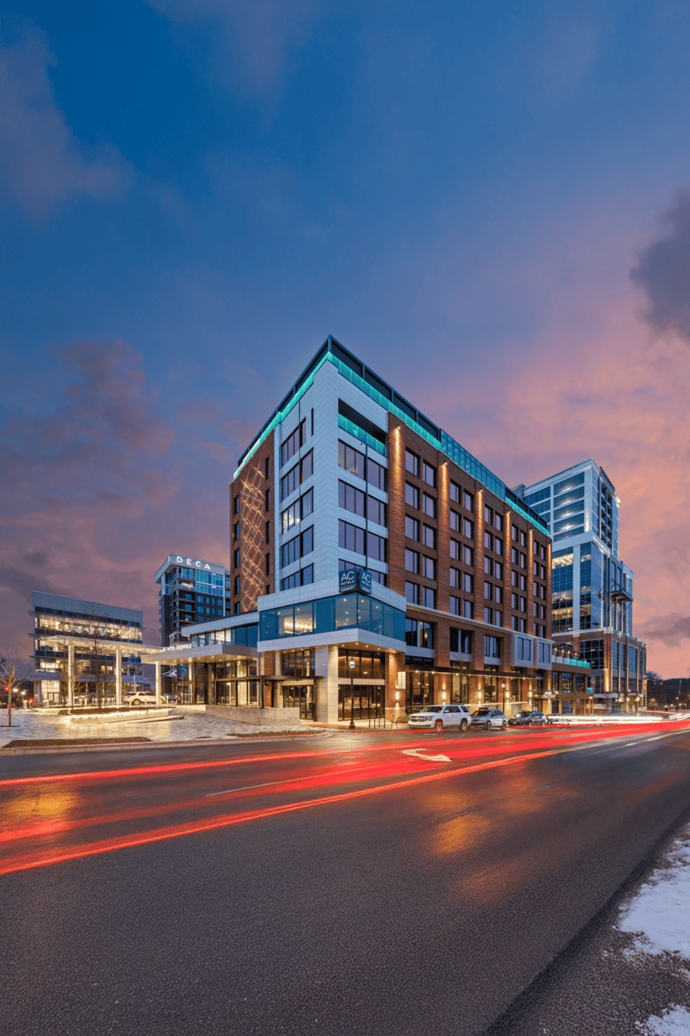 Modern urban hotel with illuminated windows and cityscape backdrop at dusk.