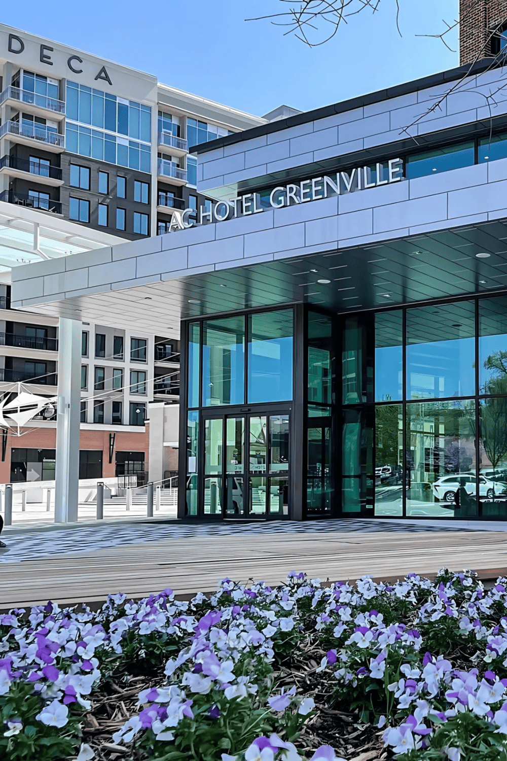 Modern hotel Greenville with glass exterior and colorful flower bed in front.