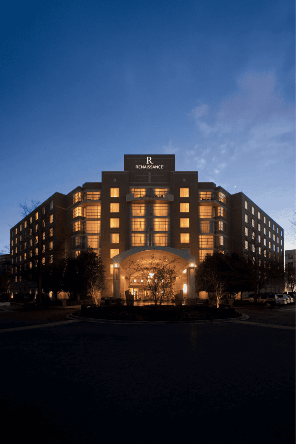 Luxury hotel exterior at dusk with illuminated windows and "Renaissance" sign, modern architecture, welcoming ambiance.
