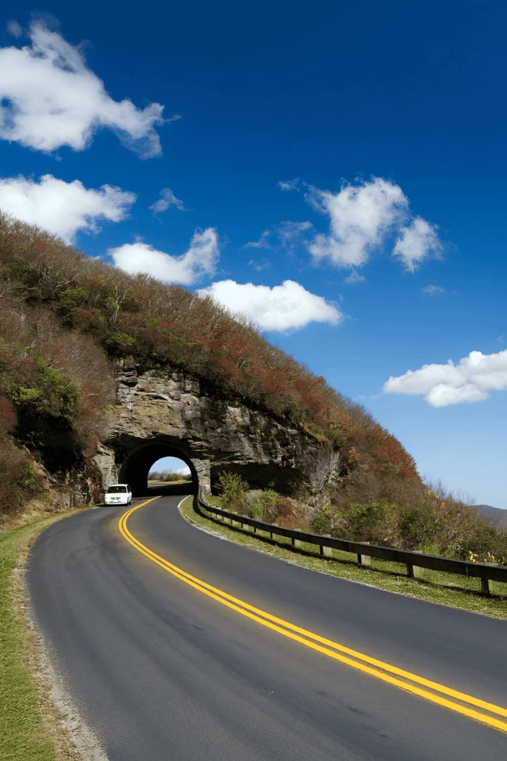 Scenic mountain road through tunnel with colorful foliage and blue sky, ideal for travel and navigation.