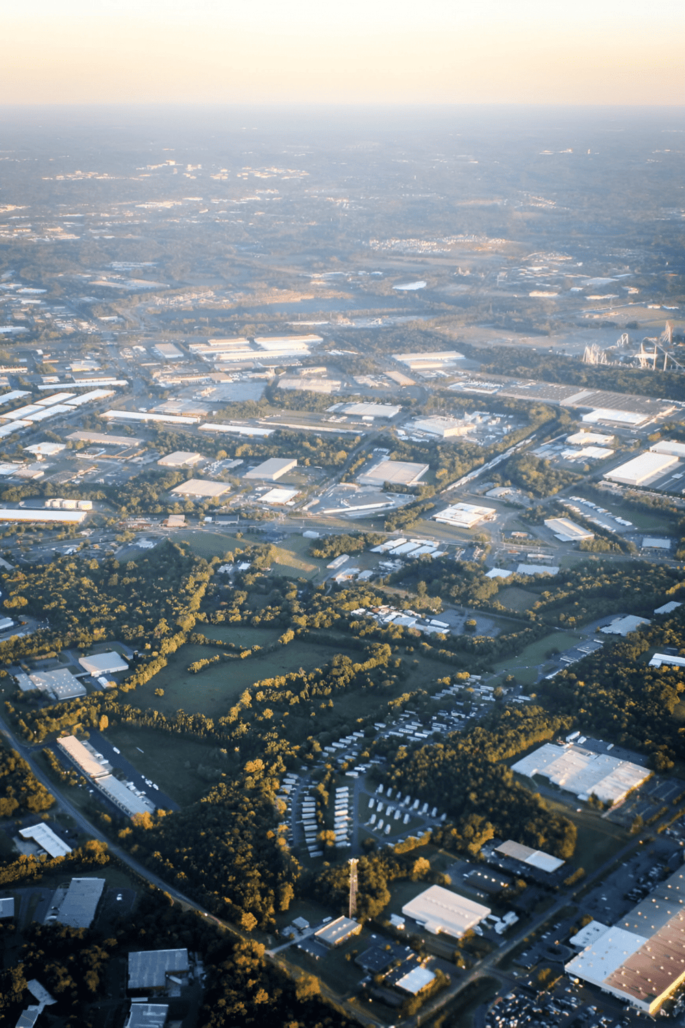 Aerial view of industrial park with warehouses and green spaces in a city landscape.