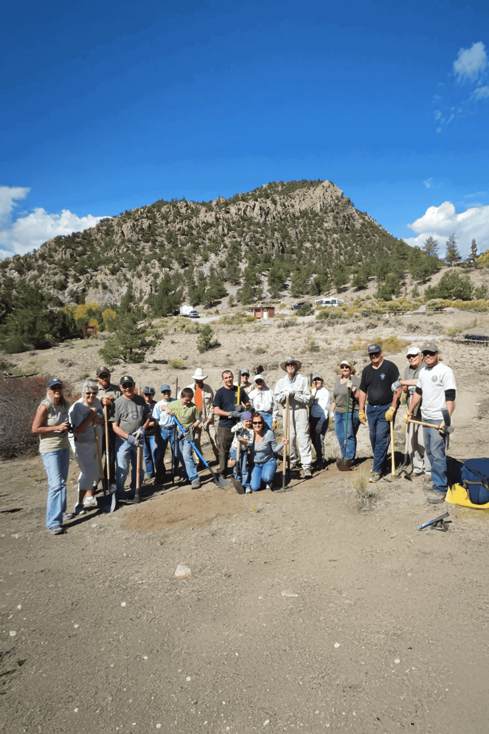 People participating in a community cleanup event outdoors with mountain scenery in the background.
